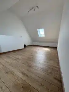 Pièce sous combles terminée : murs blancs, parquet et fenêtre de toit