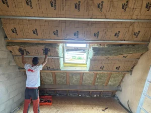 Artisan fixant l’isolant sous les rampants des combles